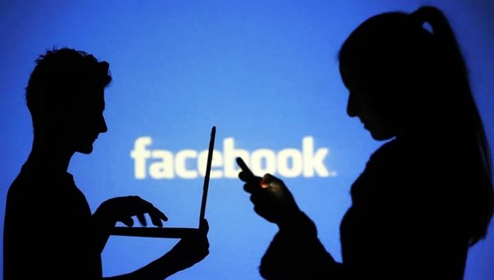 Pessoas usam eletrônicos diante de projeção do logo do Facebook